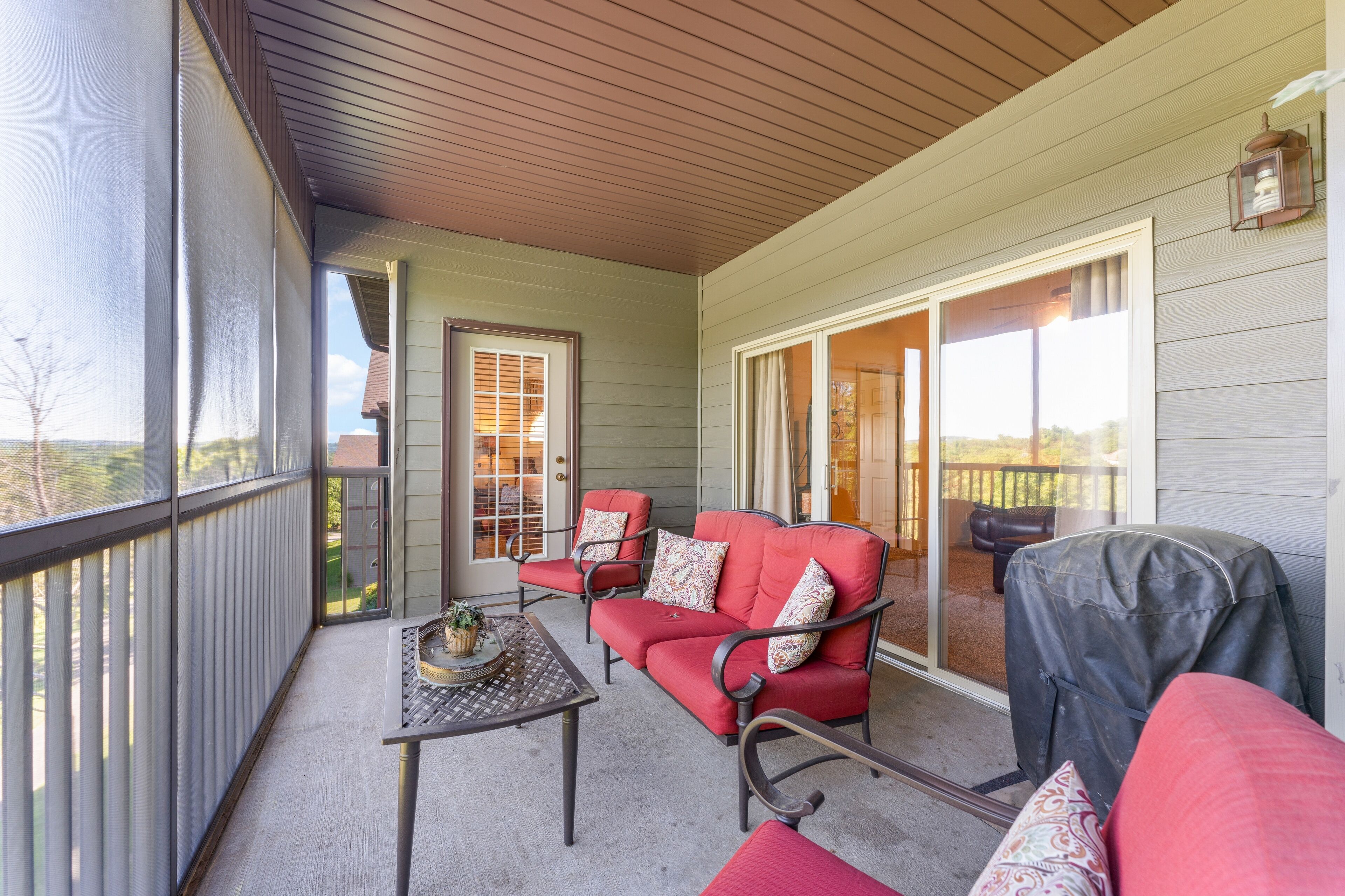 A covered porch with a red sofa set, a table with a decorative centerpiece, and a grill.