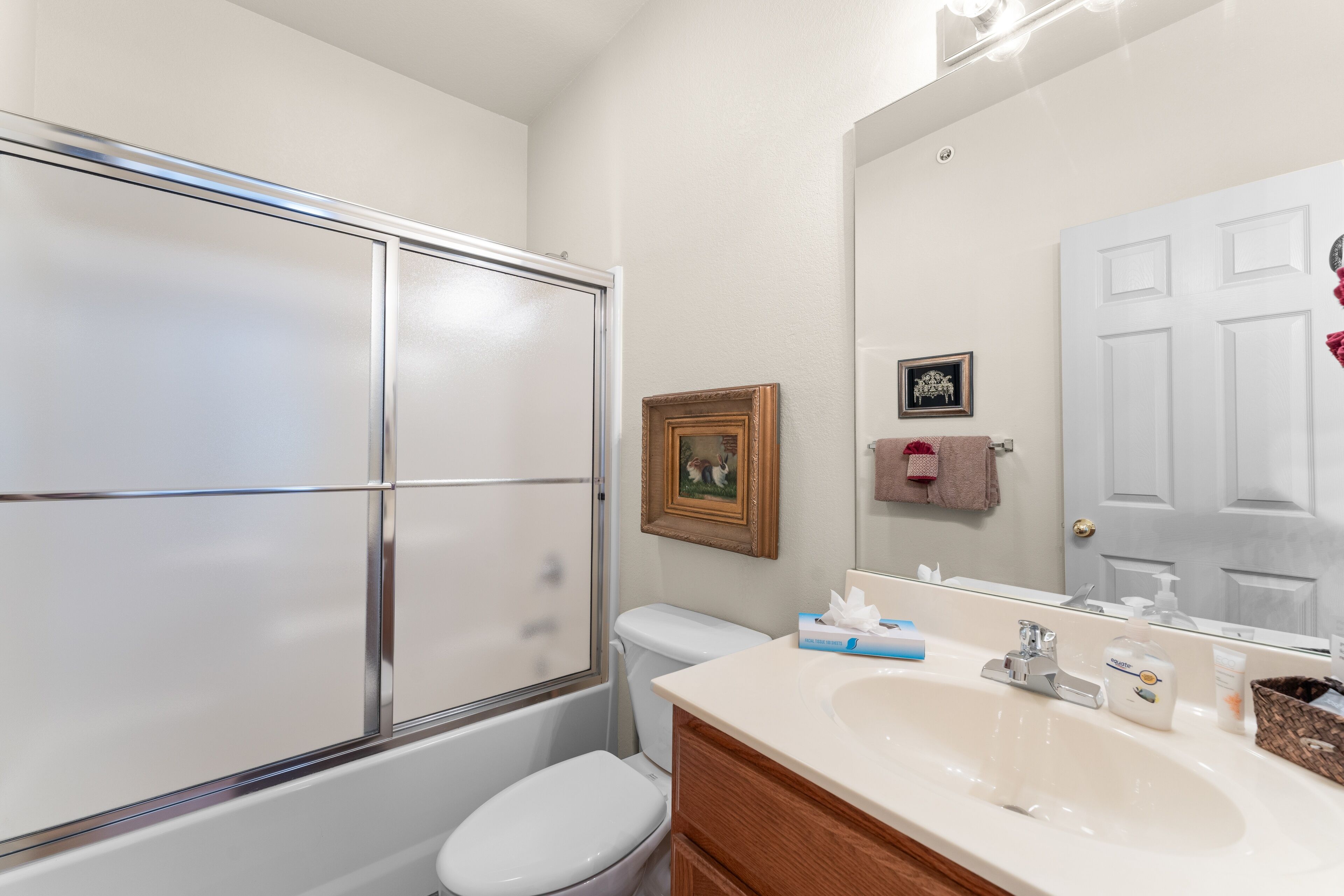 A bathroom with a glass shower enclosure, a white toilet, a vanity with a sink, and a mirror.