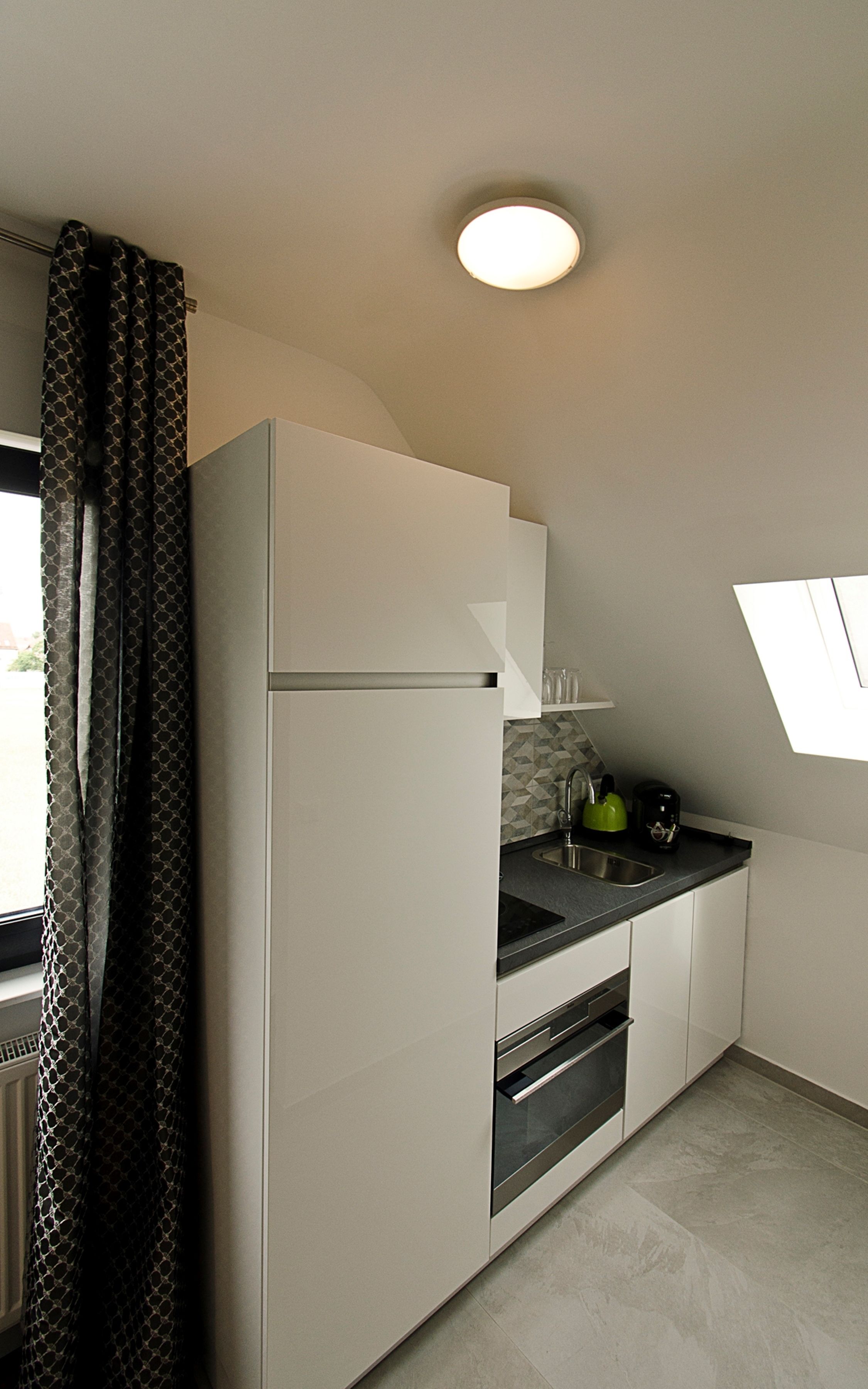 A modern kitchen with white cabinets, a black countertop, a built-in oven, and a window with a view.