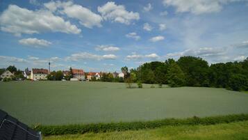 A large open field with a body of water, surrounded by trees and buildings.