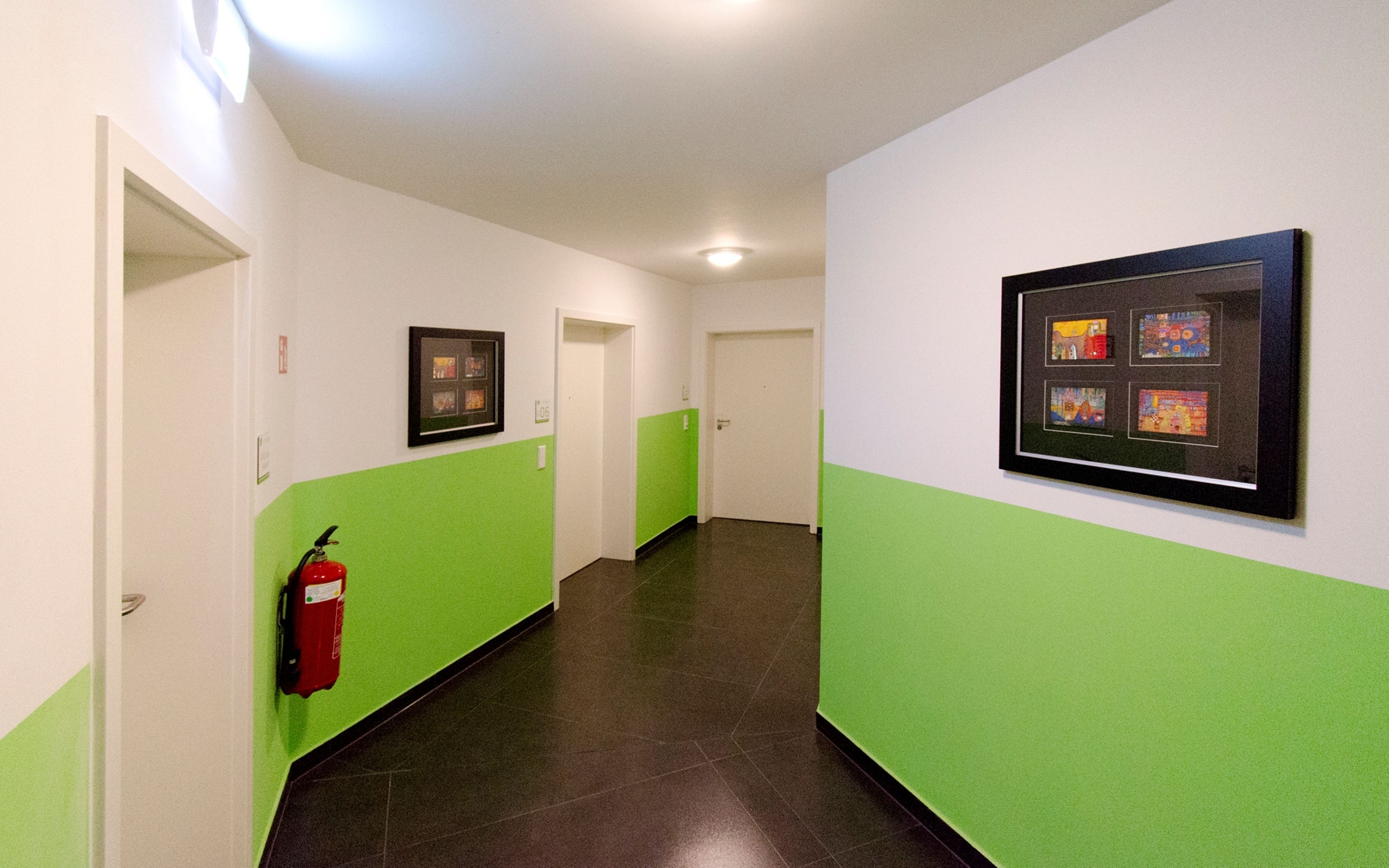 Un couloir aux murs verts, une œuvre d’art encadrée sur le côté droit et un extincteur sur le côté gauche.