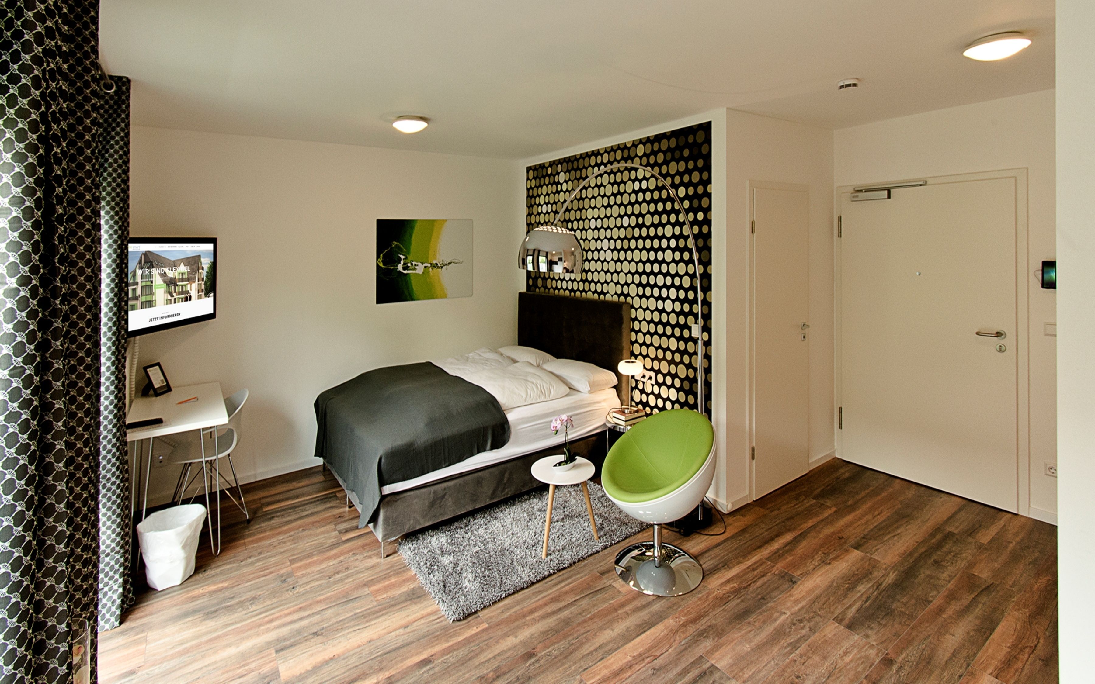 Een moderne hotelkamer met een bed, een bureau, een stoel en een groot raam.