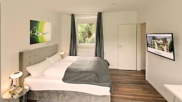 A modern bedroom with a large bed, a bedside table with a lamp, a framed picture on the wall, and a window with curtains.