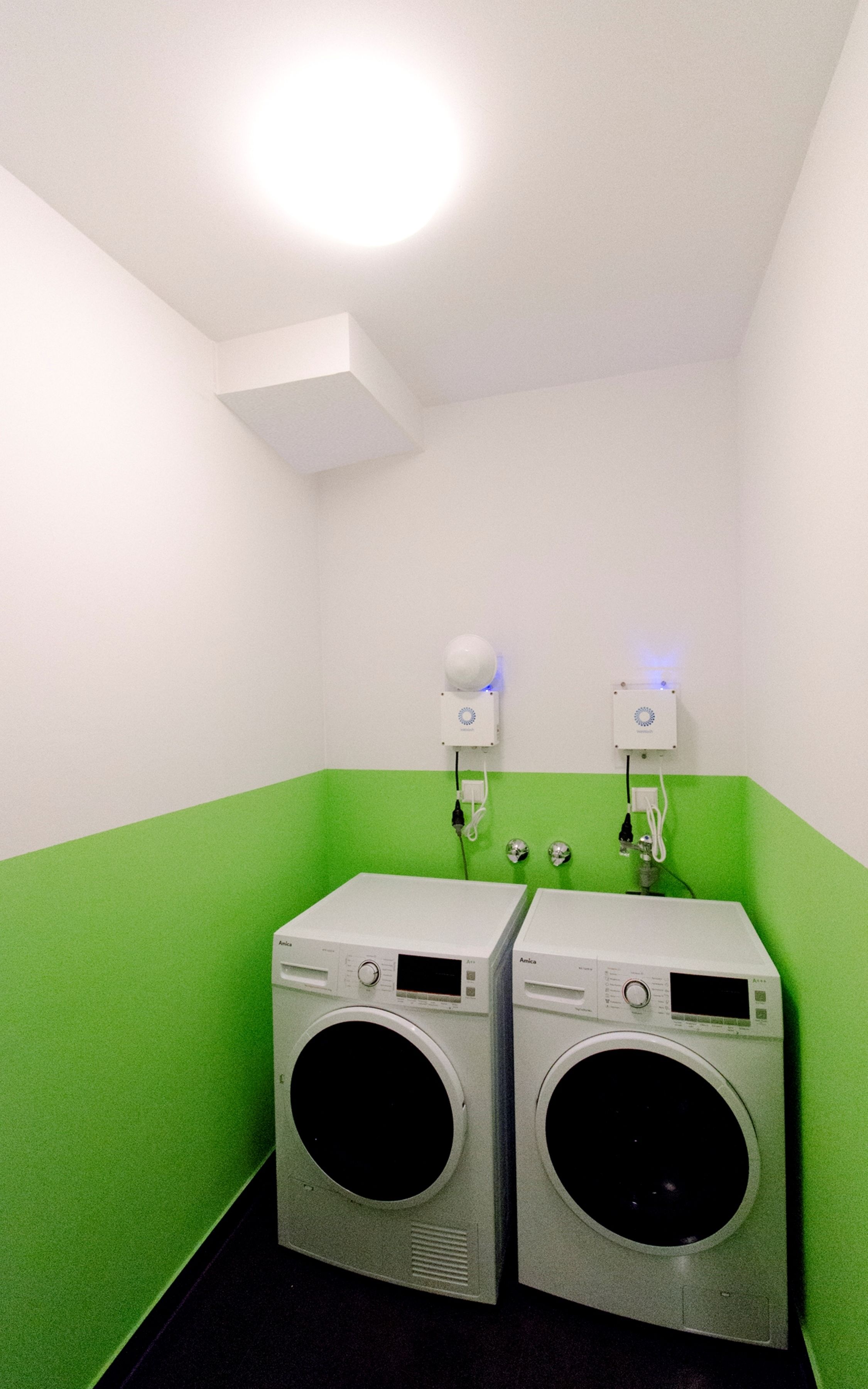 A laundry room with two washing machines, a green wall, and a white ceiling.