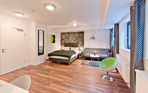 A modern hotel room with a bed, a sofa, a chair, a desk, and a window. - Eco Smart Apartments Nürnberg Süd (Nuremberg)