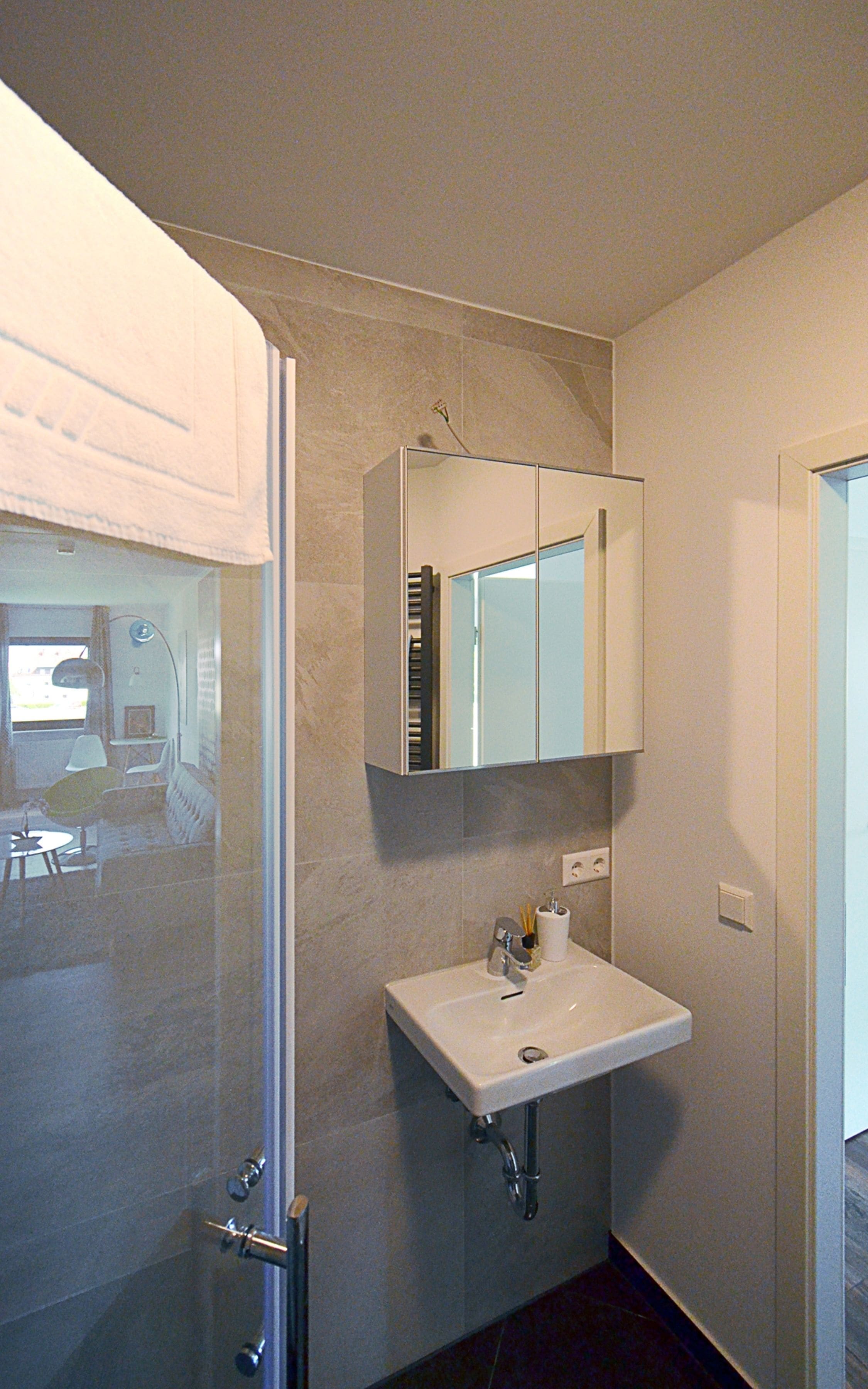 A bathroom with a glass shower enclosure, a white sink, and a mirror above it.