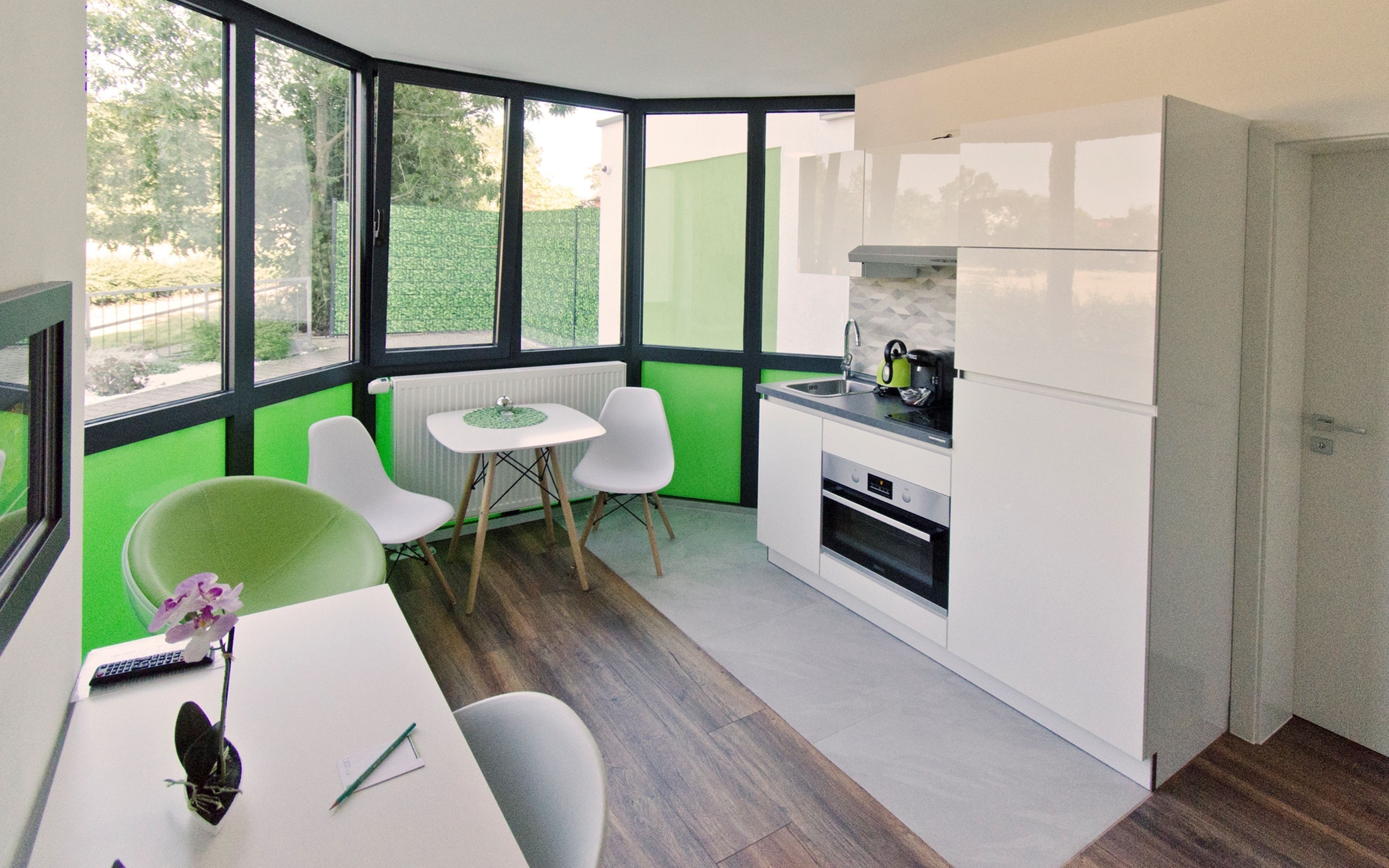 Een moderne keuken met witte kasten, een eethoek met een kleine tafel en twee stoelen, en grote ramen met uitzicht op de omgeving.