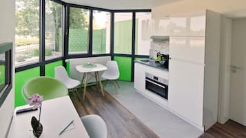 A modern kitchen with white cabinets, a dining area with a small table and two chairs, and large windows offering a view of the outdoors.