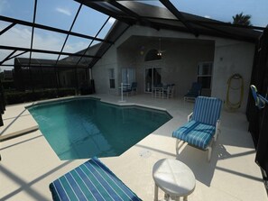 An indoor swimming pool with lounge chairs and a table, surrounded by a covered patio area. - Cumbrian Lakes 20 (Kissimmee)