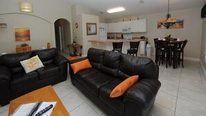 Uma sala de estar com dois sofás de couro preto, uma mesa de centro de madeira e um ventilador de teto.