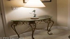 Uma mesa de vidro com uma luminária decorativa e um cartaz informativo emoldurado na parede.