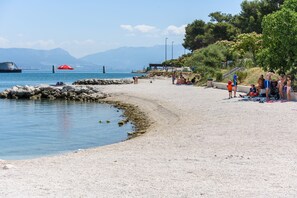 Une plage avec un rivage rocheux, un parasol rouge et des gens qui se détendent.