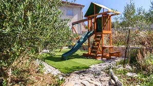 Un terrain de jeux avec un toboggan et une structure d’escalade, entouré de verdure et bordé d’un chemin en pierre.
