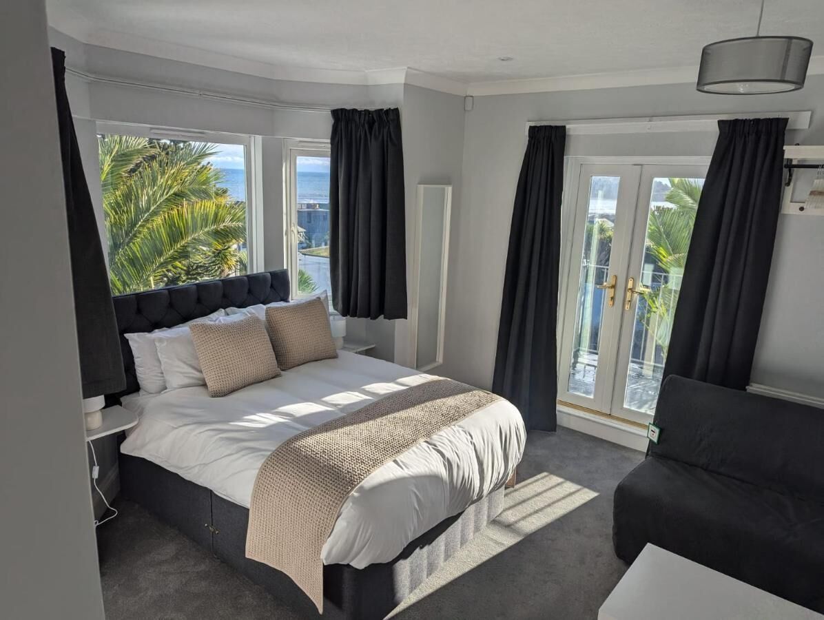 Ein Schlafzimmer mit einem großen Bett, dunklen Vorhängen, Blick ins Freie und einem Balkon.