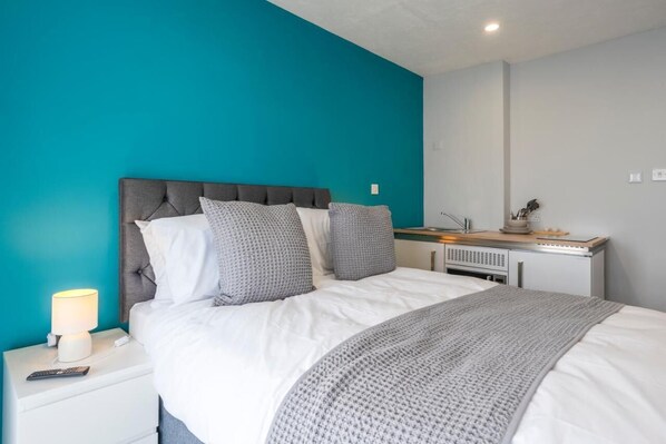 A bedroom with a bed, a nightstand, a desk, and a lamp. - Fieldhead Hotel (Looe)