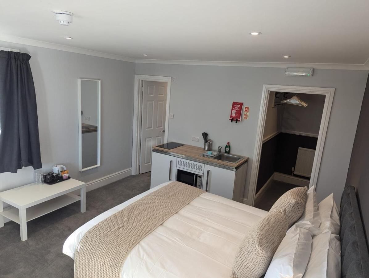 A hotel room with a bed, a desk with a sink, a mirror, a bench, and a coat rack.