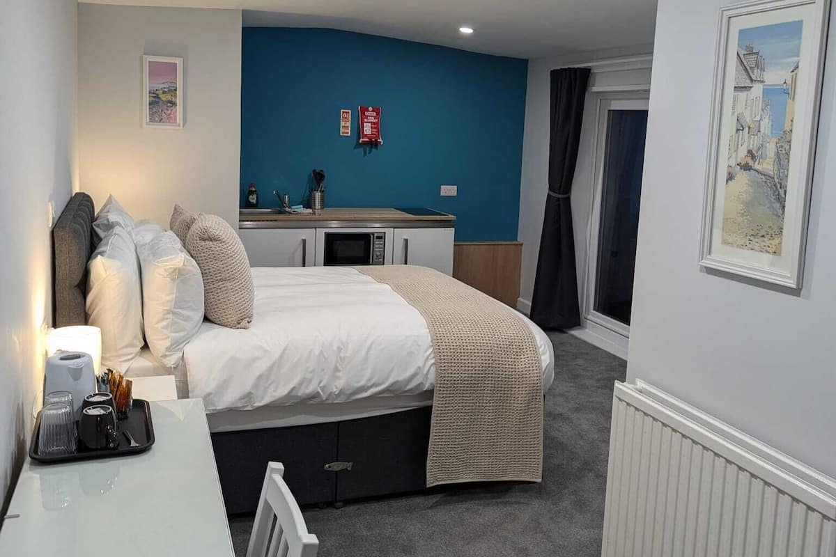 Quarto de hotel compacto com cama, pequena escrivaninha, cozinha compacta e vista para a rua.