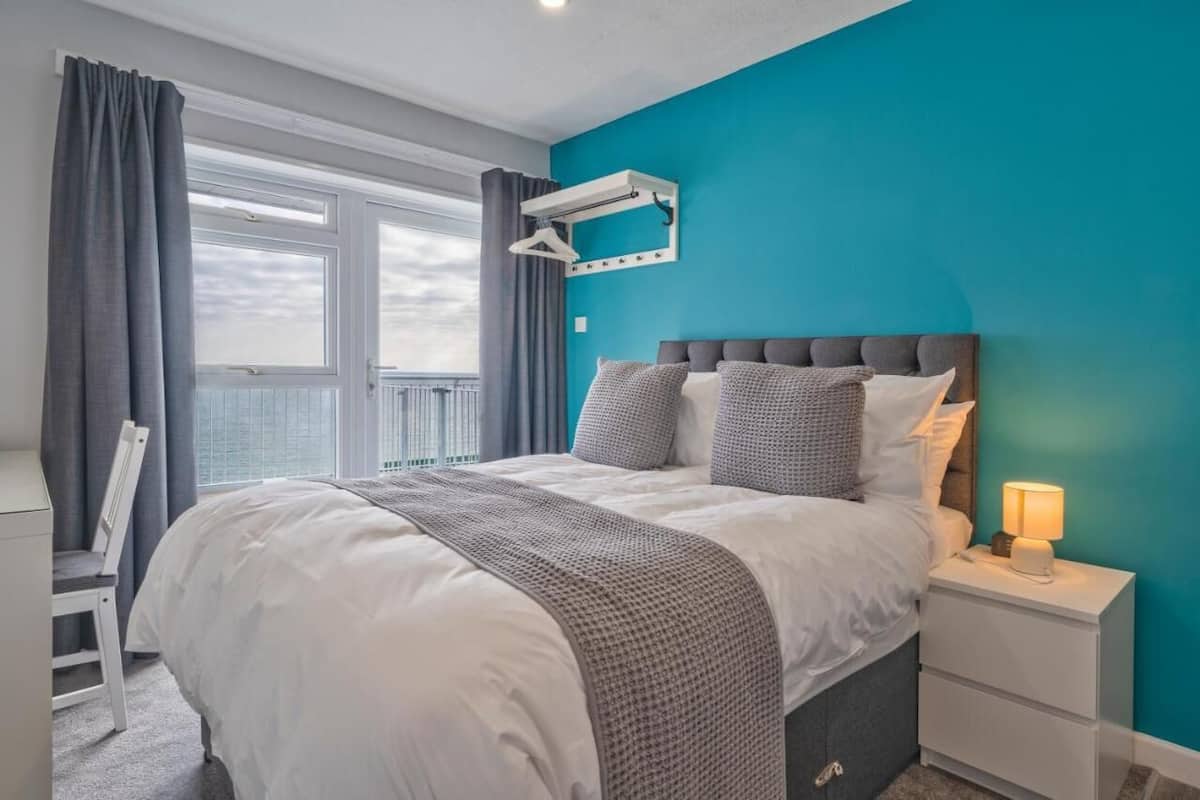 Quarto com cama, mesa de cabeceira e janela com cortinas.