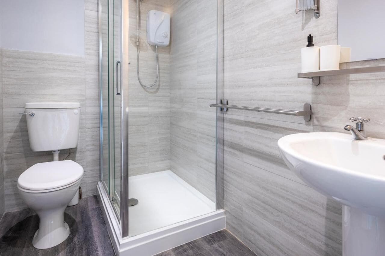 A modern bathroom with a glass-enclosed shower, a white toilet, and a sink with a mirror above it.