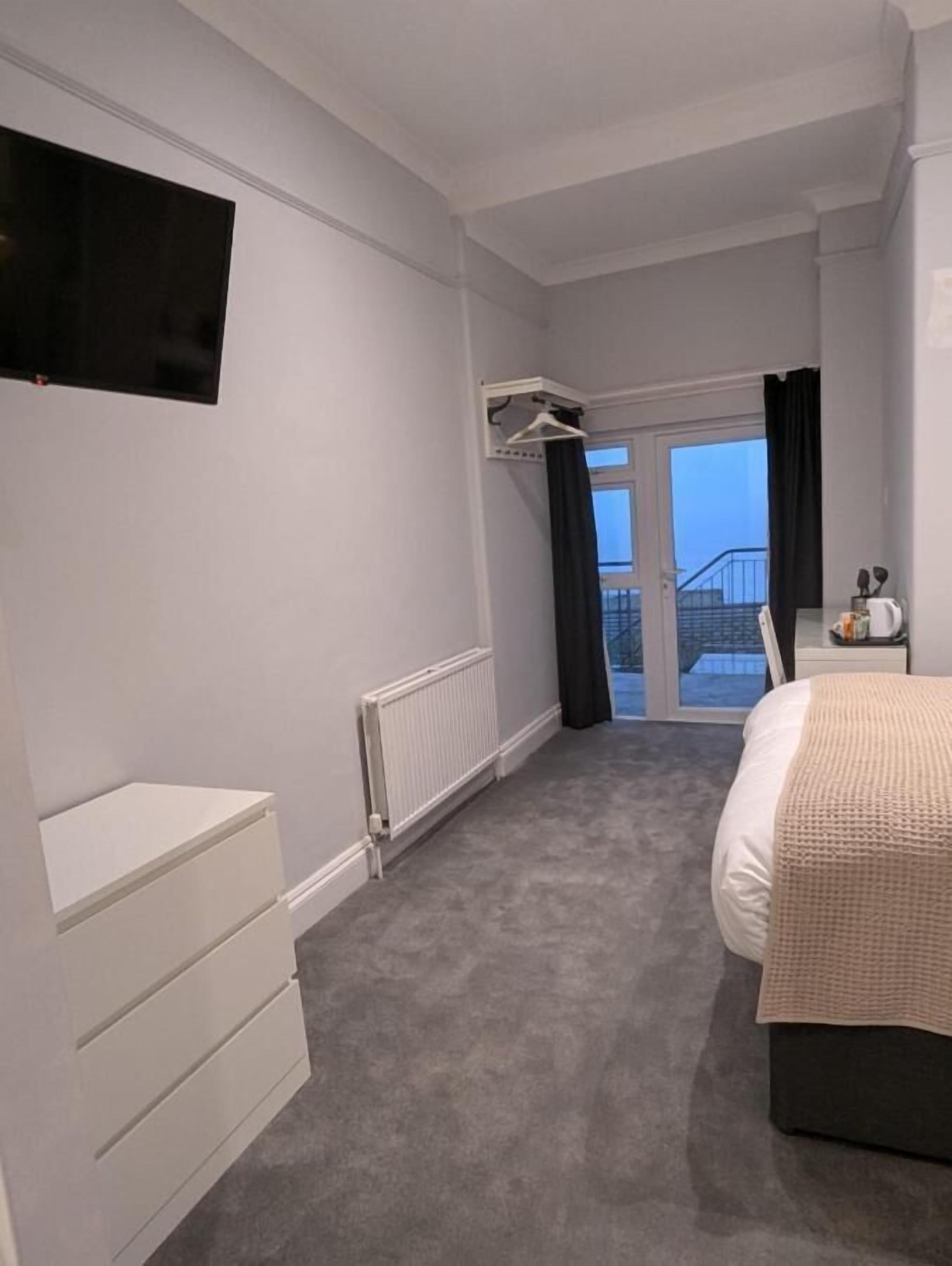 Ett modernt hotellrum med en stor säng, en tv som är monterad på väggen, en byrå och utsikt över balkongen.