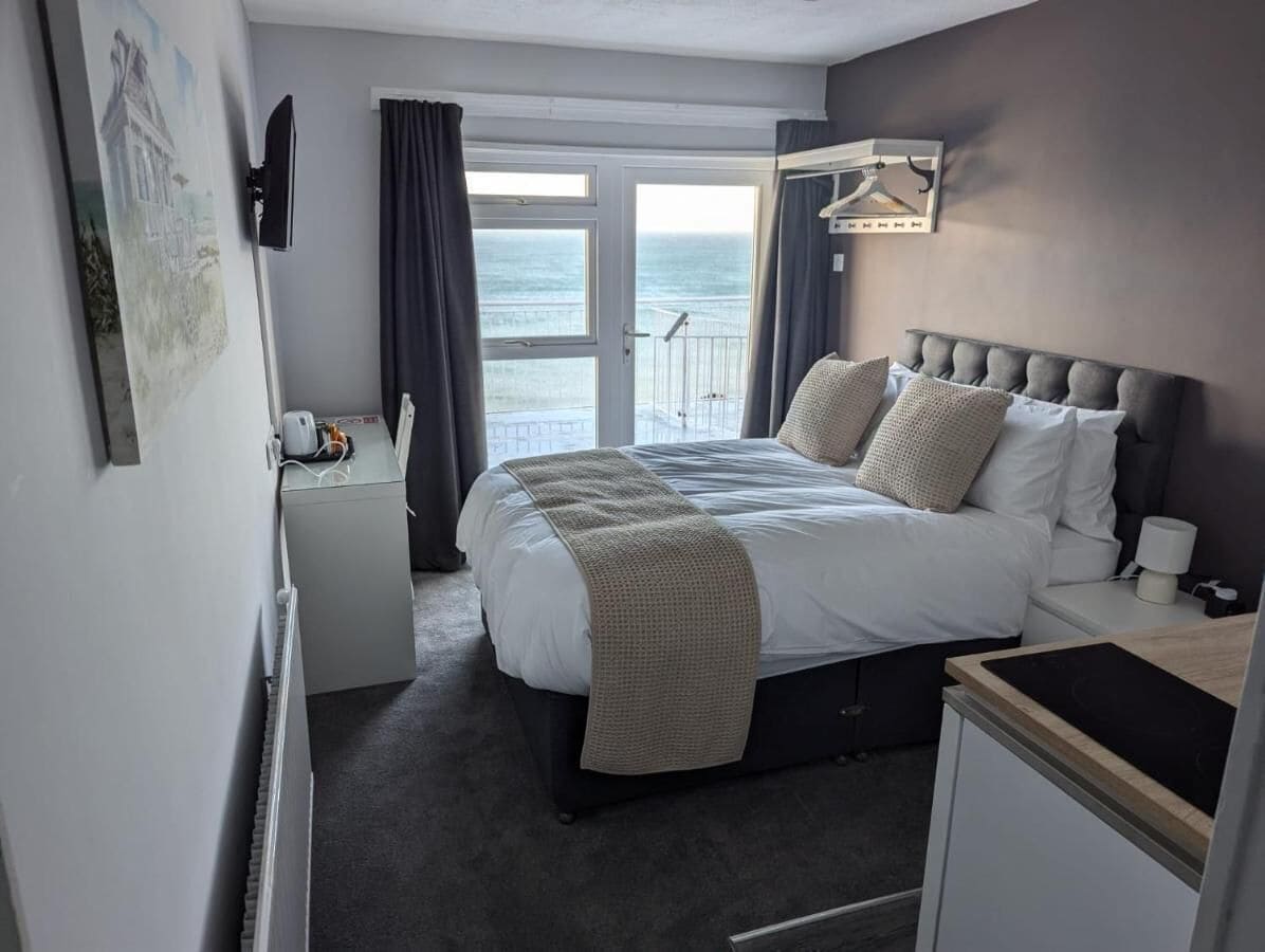 Une chambre d’hôtel avec un grand lit, une table de chevet, un bureau et une vue sur la mer par une grande fenêtre.