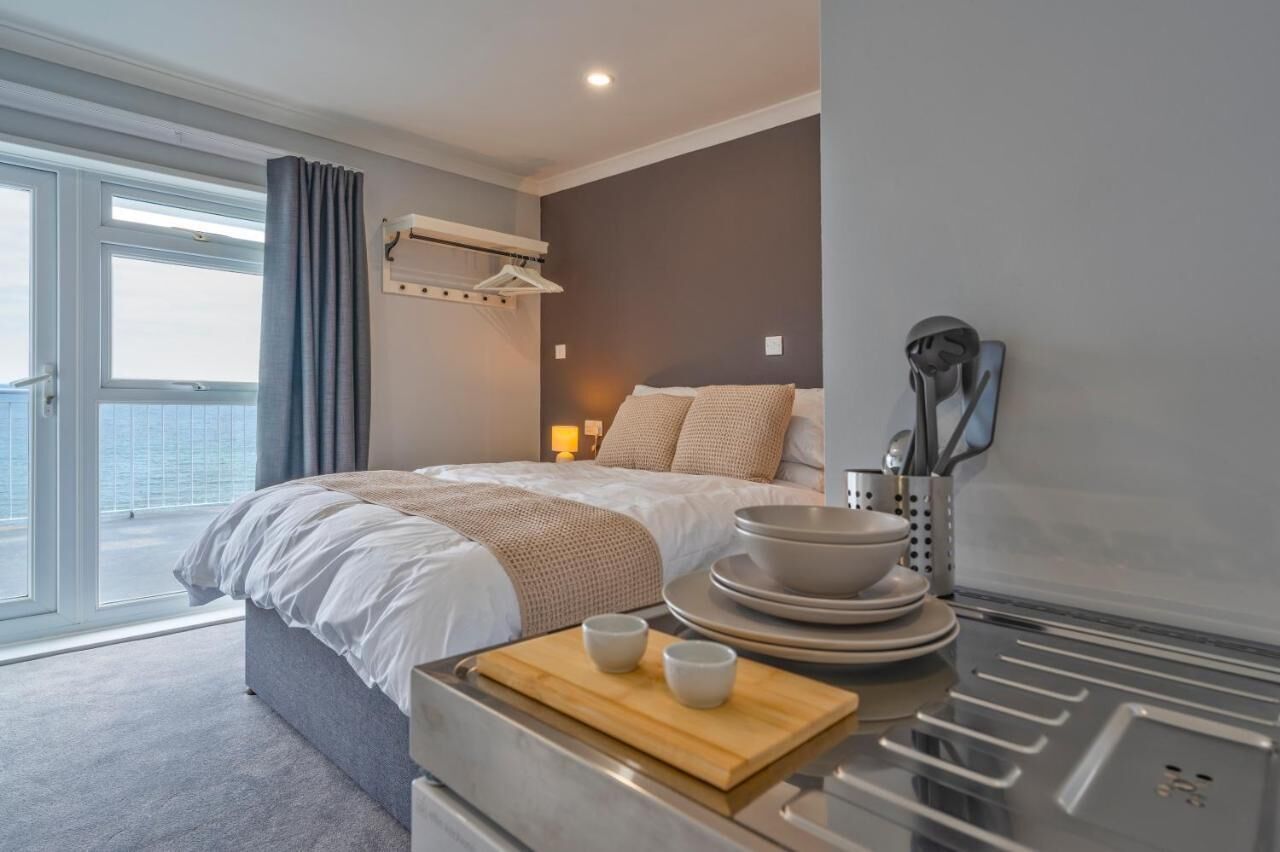 Une chambre d’hôtel moderne dotée d’un grand lit, d’un coin repas avec une table et des chaises, et offrant une vue sur la ville grâce à de grandes fenêtres.