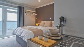 Une chambre d’hôtel moderne dotée d’un grand lit, d’un coin repas avec une table et des chaises, et offrant une vue sur la ville grâce à de grandes fenêtres.