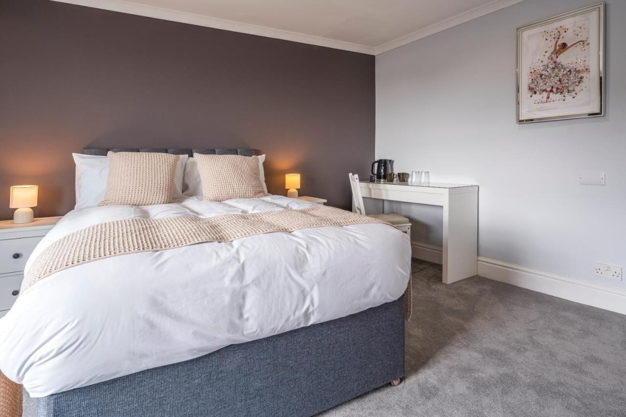 A bedroom with a bed, bedside lamps, a desk, and a coffee maker.