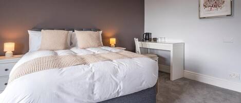 A bedroom with a bed, bedside lamps, a desk, and a coffee maker.