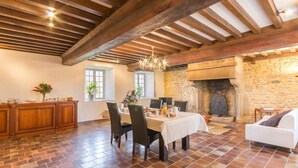 Un comedor amplio con chimenea de piedra, vigas de madera y suelo de baldosas.