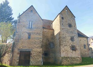 Un edificio histórico de piedra con una gran torre central y una sección más pequeña con puerta de madera.