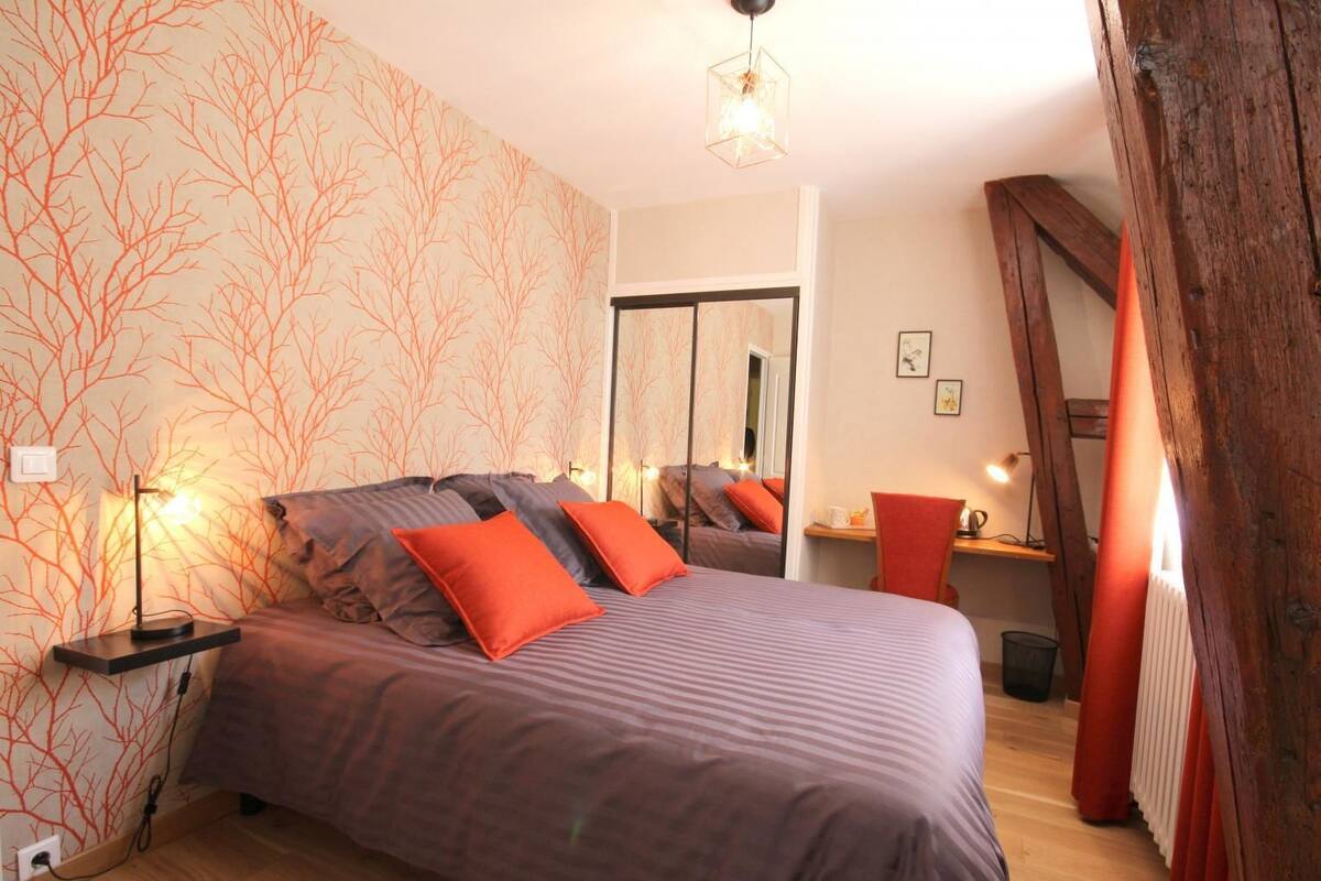Quarto com cama, mesas de cabeceira, espelho e cadeira de madeira.