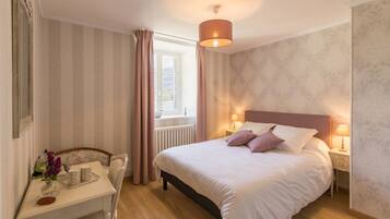 A bedroom with a bed, bedside lamps, a window with curtains, a small table with a vase and a tray, and a chair.
