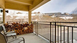 A balcony with a stack of firewood, a chair, and a view of a snowy landscape with buildings in the background.