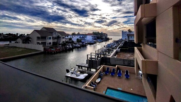 A marina with boats docked, a swimming pool, and a view of the waterfront with buildings. - Landfall Towers 34 Minium 1 Bedroom Condo by RedAwning (South Padre Island)