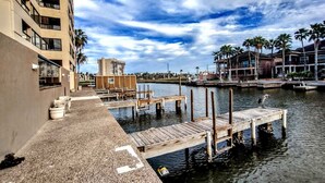 A waterfront property with a dock, a building with multiple floors, and a clear sky. - Landfall Towers 34 Minium 1 Bedroom Condo by RedAwning (South Padre Island)