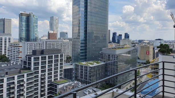 A high-rise building with a modern glass facade, surrounded by other high-rise buildings and a clear sky. - Chopin Apartments Eco (Warsaw)