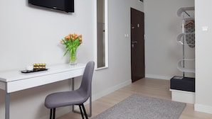 A modern room with a white desk, a grey chair, a flat-screen TV, a vase of flowers, and a wardrobe. - Chopin Apartments Eco (Warsaw)