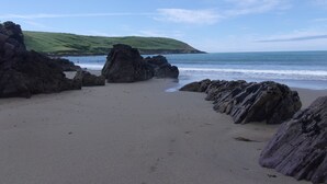 A beach with large rocks and a grassy hill in the background.