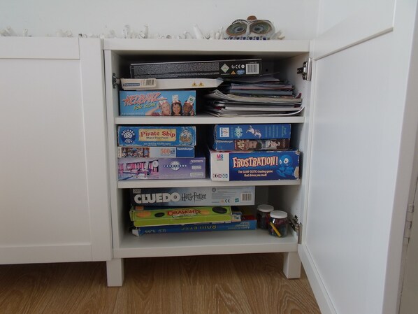 A white cabinet with shelves containing various board games and puzzles.