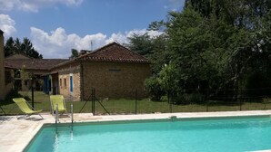 A rectangular swimming pool with a tiled edge, surrounded by a stone deck. There are two yellow lounge chairs and a metal ladder leading into the pool.