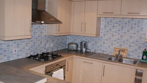 Une cuisine avec des meubles de rangement en bois clair, une cuisinière à gaz, un grille-pain, une bouilloire et un évier.
