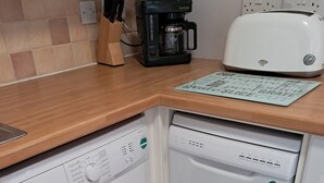 A compact kitchen with a washing machine, a coffee maker, and a toaster. - Ornum Cottage (Beauly)