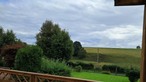 A wooden deck with a view of a green field and trees. - Ornum Cottage (Beauly)