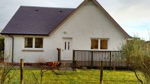 Una casa a un piano con tetto in tegole scure, pareti esterne bianche e un portone con un piccolo portico.