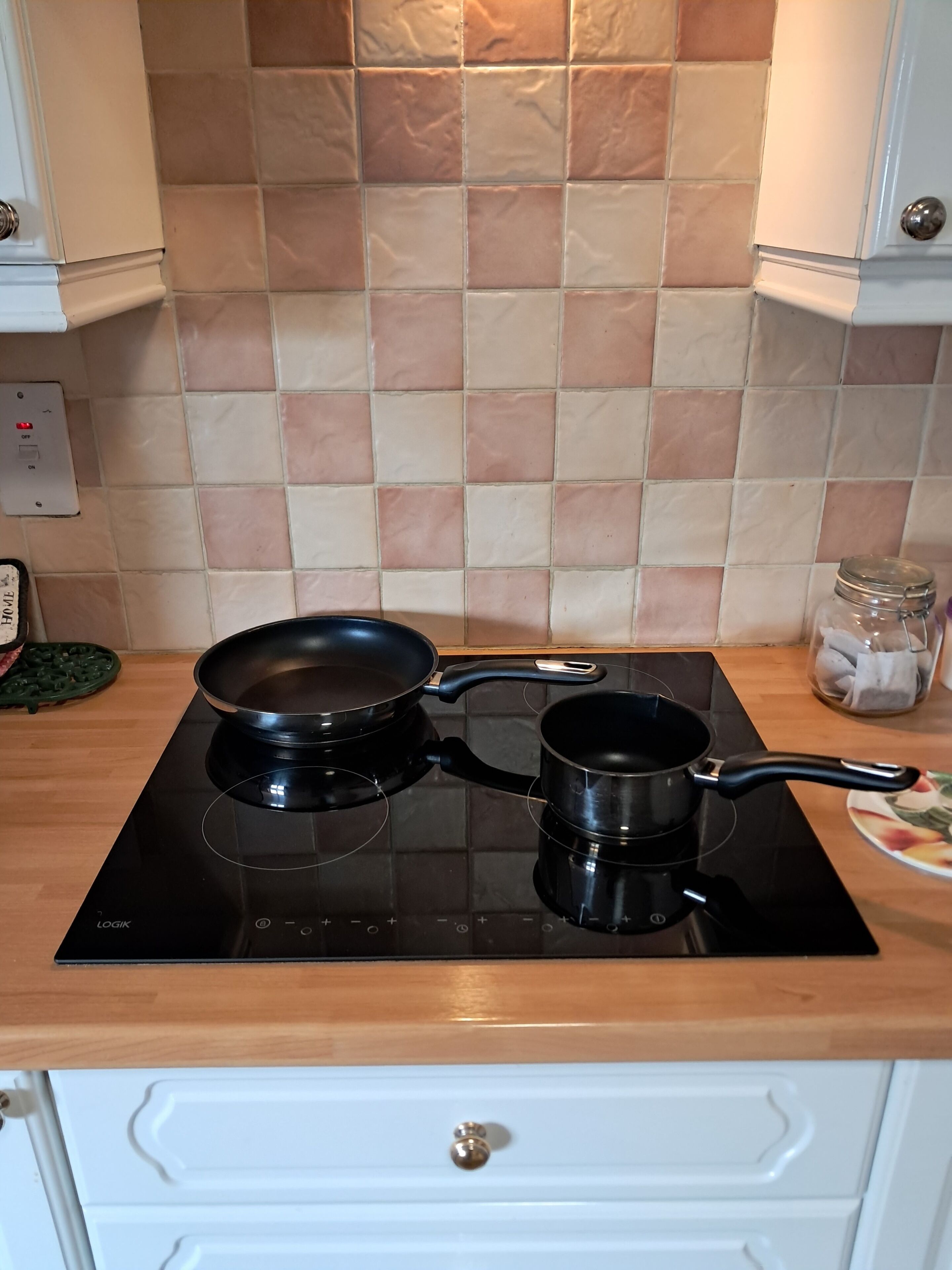 A kitchen with a black induction cooktop, two black pots, and a green spatula on the counter.