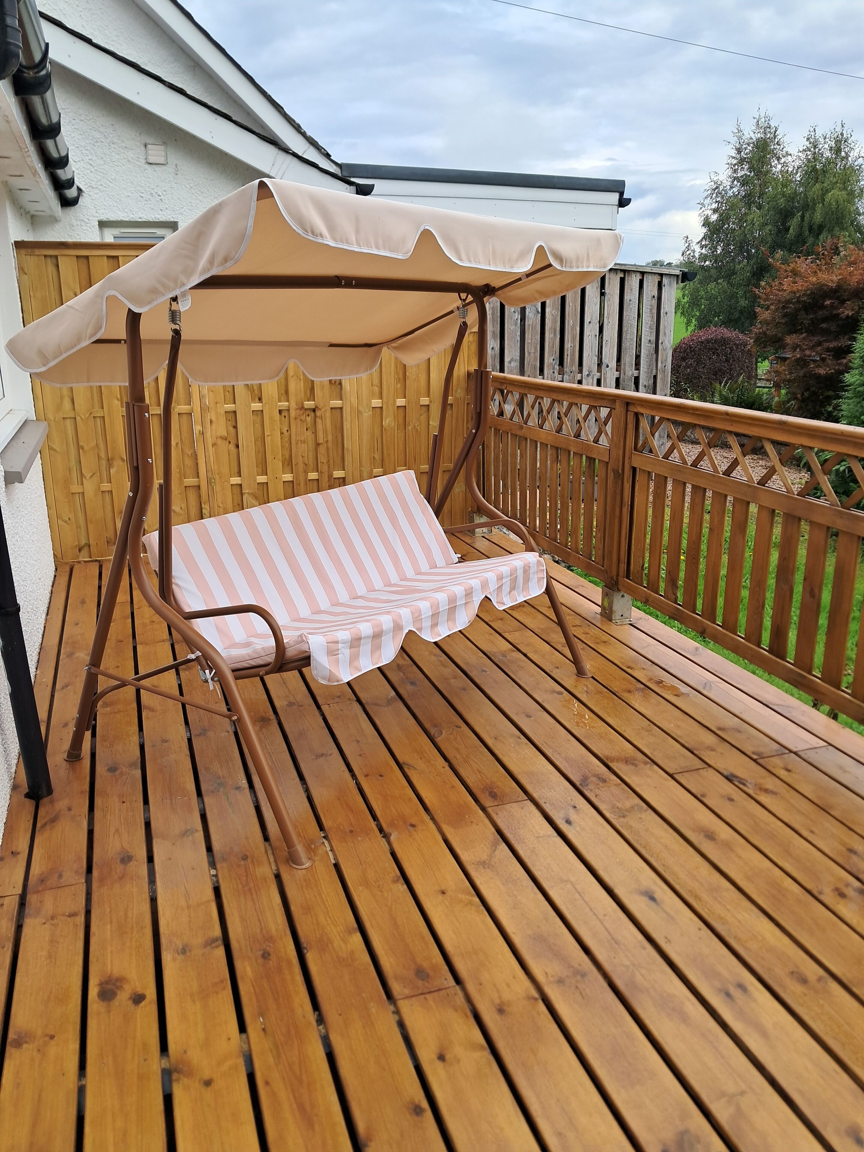 A wooden deck with a striped lounge chair and a canopy.