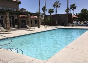 A rectangular swimming pool with clear blue water, surrounded by a tiled deck. There are lounge chairs and a stone pillar structure.