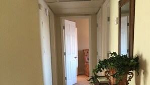 Ein Korridor mit Holzboden, einer Tür am Ende, einer Bank mit Pflanze und einem Spiegel an der Wand.