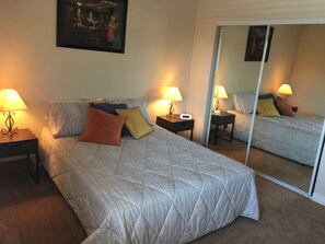 A hotel room with a large bed, two bedside tables with lamps, a nightstand, a mirror, and a framed picture on the wall.